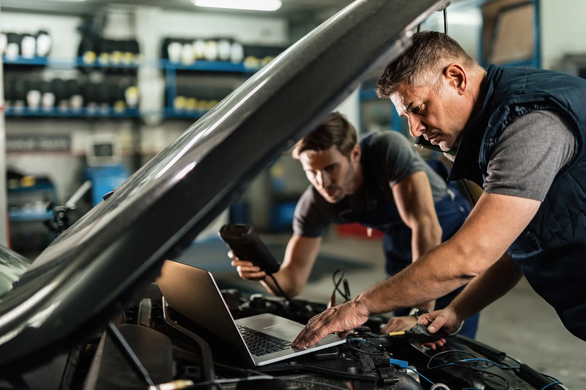 mecanicien automobile utilisant ordinateur portable cooperant collegue tout effectuant diagnostic voiture dans atelier reparation